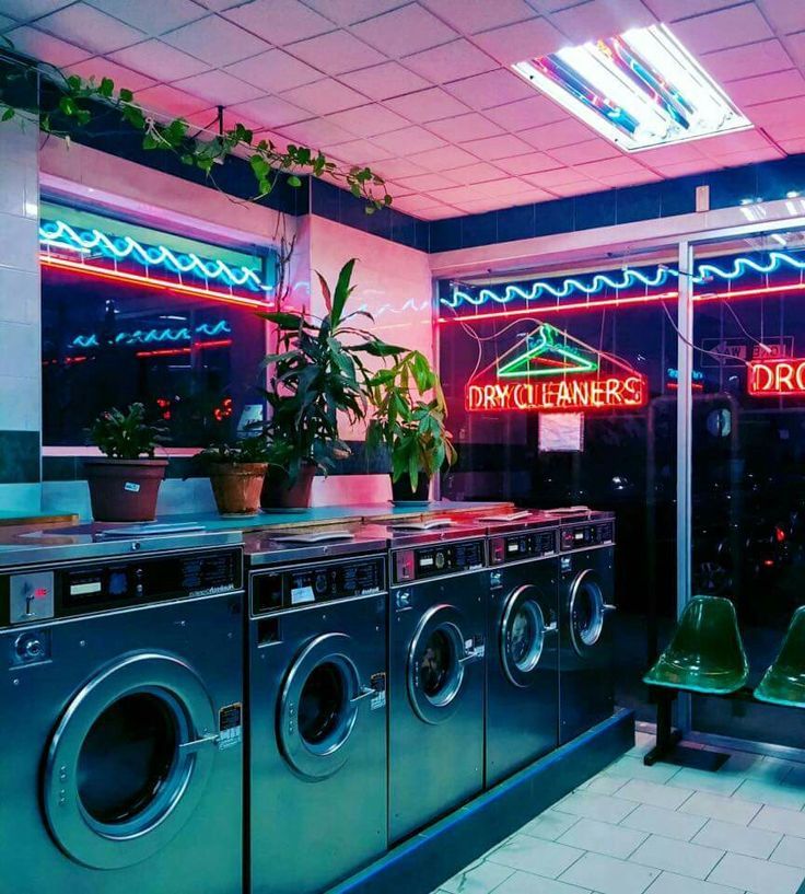 a laundry room filled with washers and dryers next to a neon lit sign