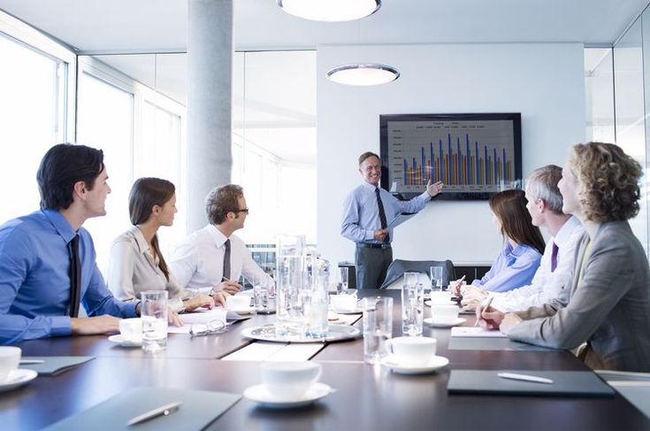 a group of business people sitting around a conference table in front of a projector screen