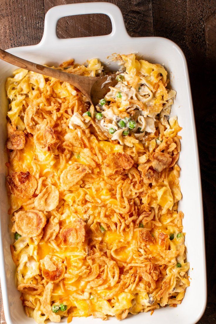 a casserole dish with chicken and cheese in it on a wooden table next to a spoon