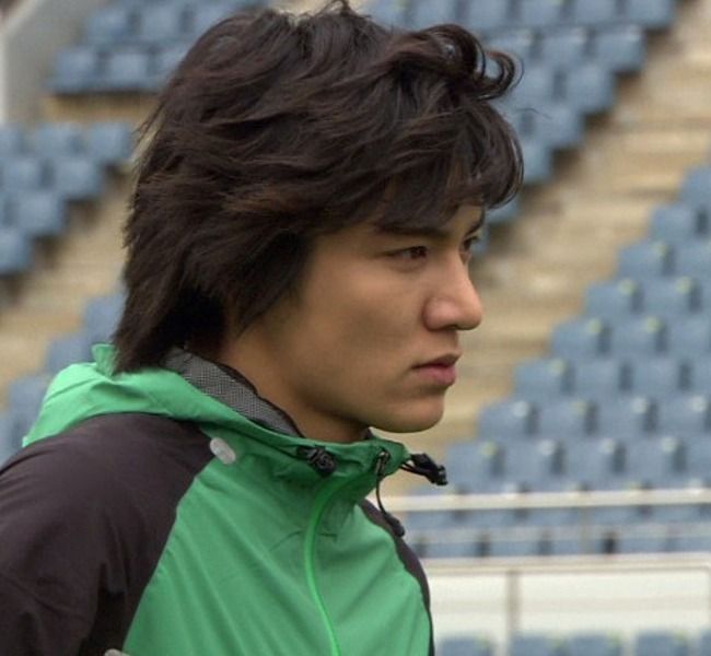 a young man in a green and black jacket standing next to an empty bleachers