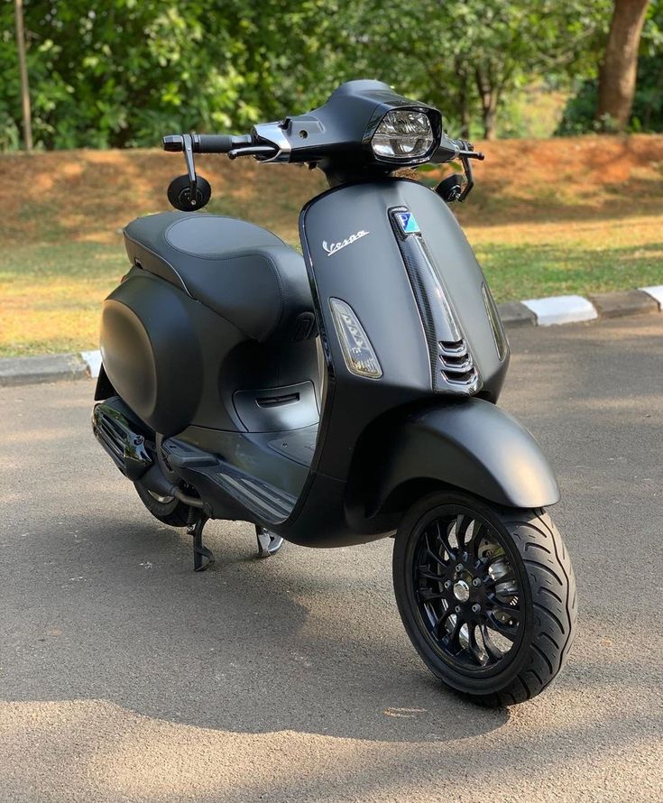 a black scooter parked on the street in front of some grass and trees