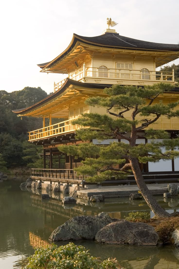 a tall yellow building sitting on top of a lush green hillside next to a lake