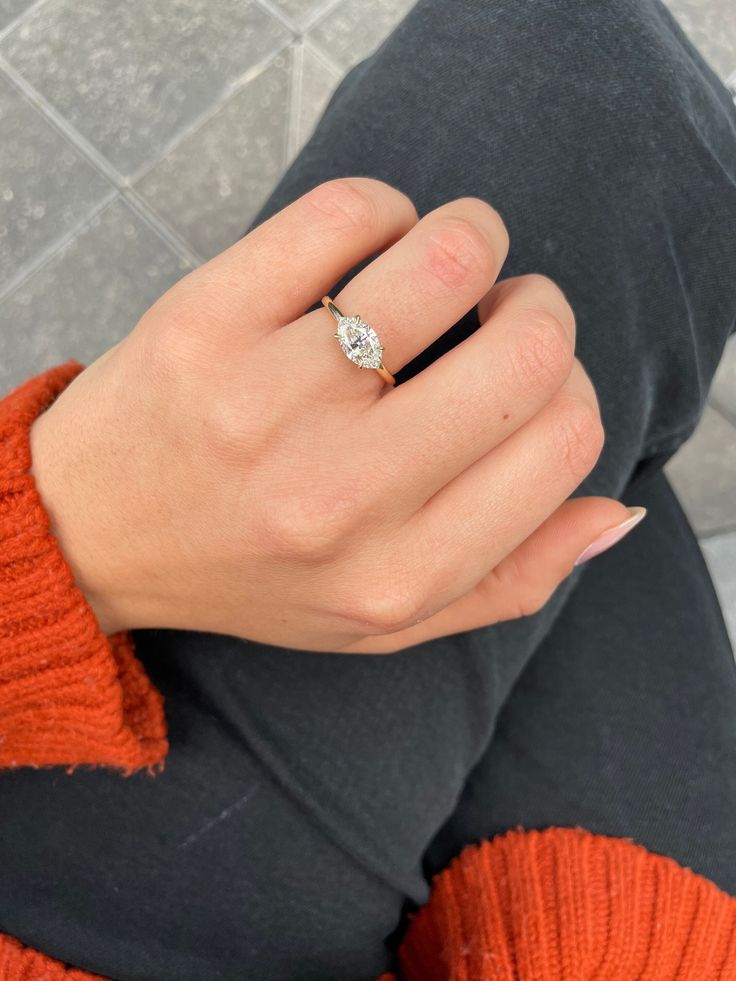 a woman's hand with a diamond ring on top of her finger and an orange sweater