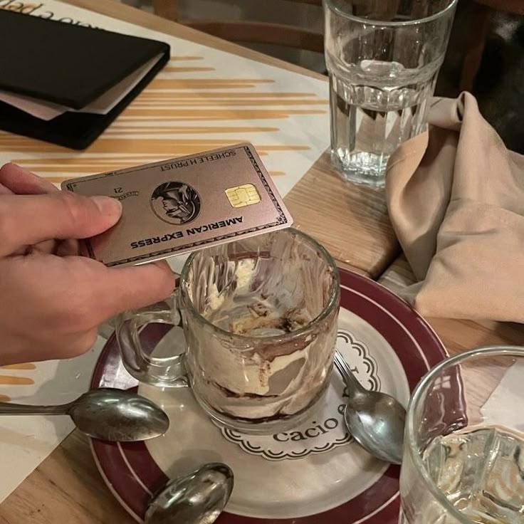 a person is holding a credit card over a cup of ice cream on a plate