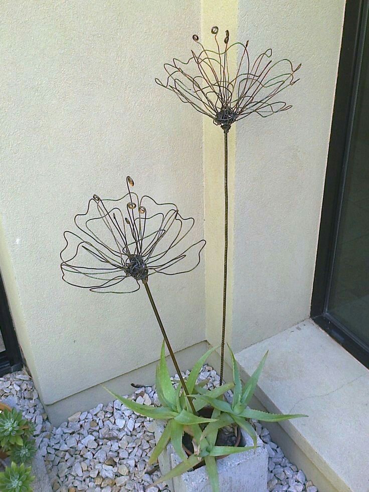 two metal flowers sitting next to each other on a rock garden bed in front of a building