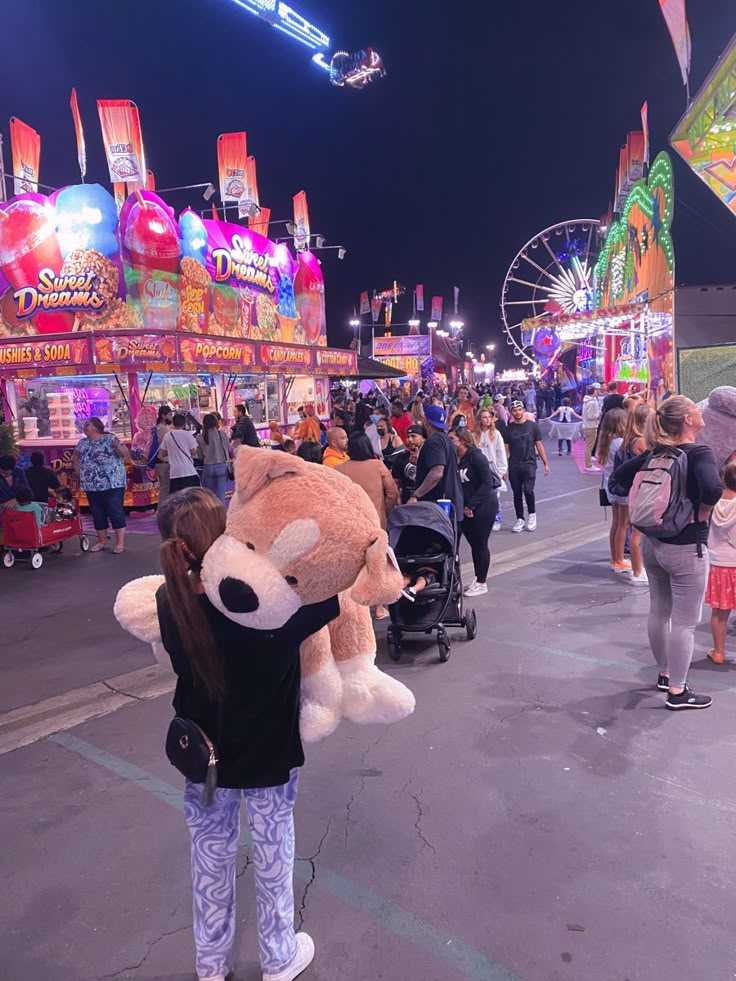 a person holding a large teddy bear in the middle of a street at an amusement park