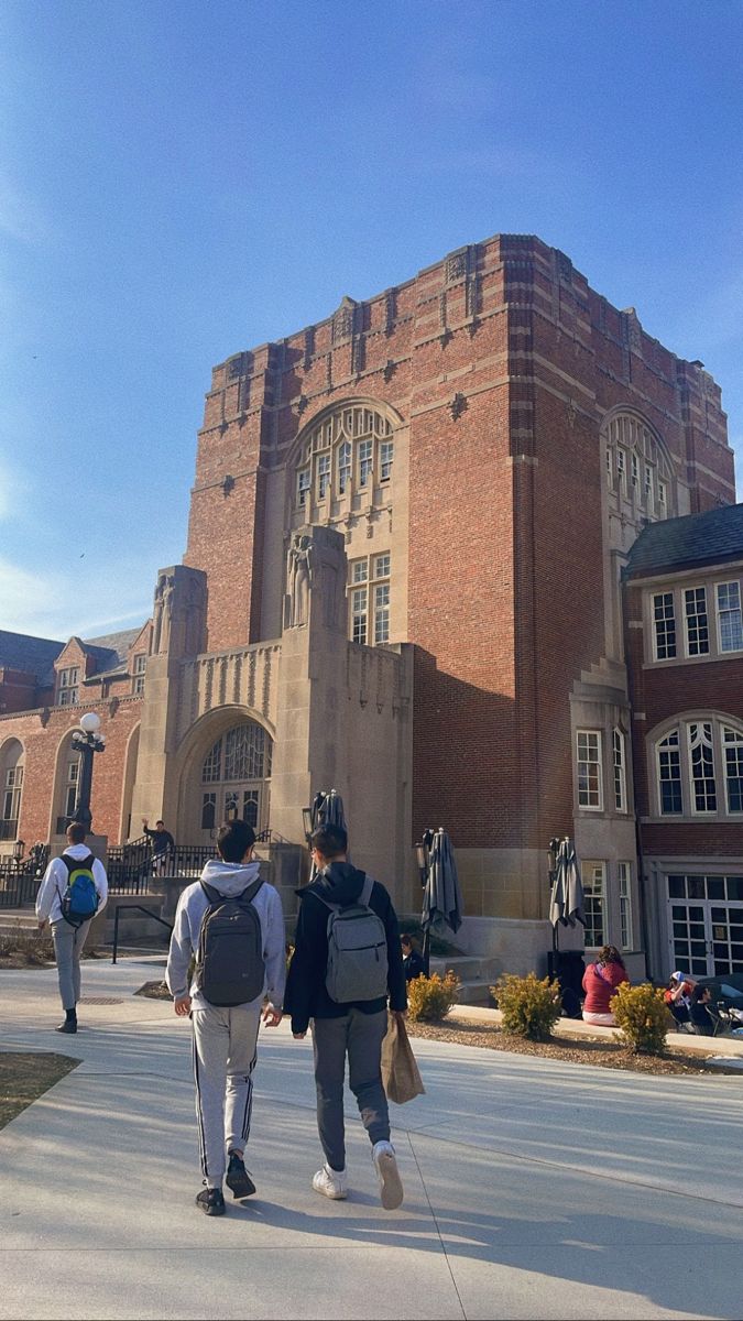 two people walking in front of a large building on a sunny day with blue skies