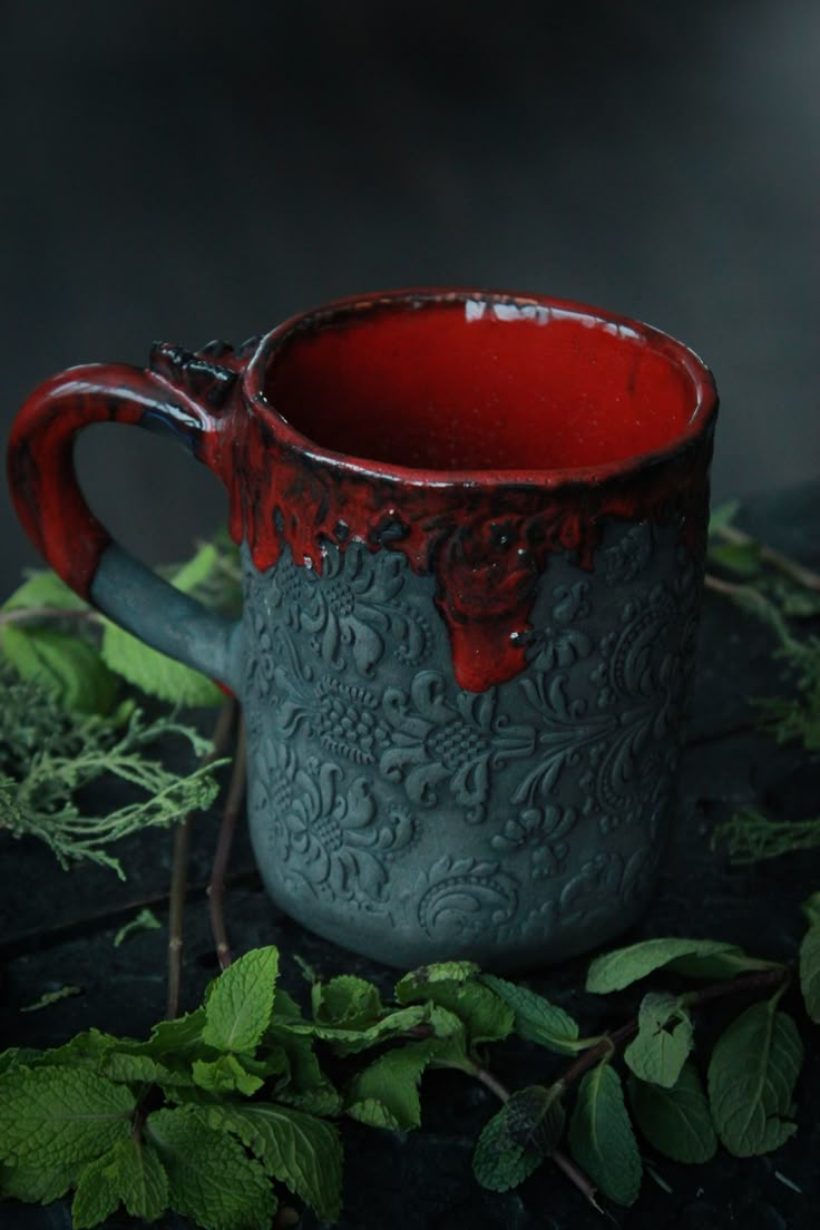 a red and black mug sitting on top of green leaves in front of a dark background