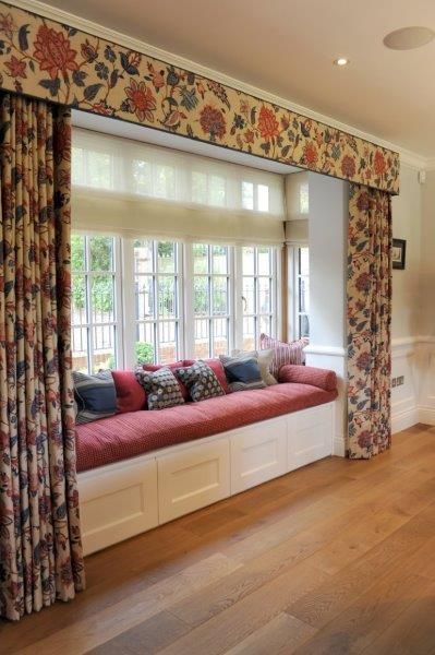 a living room filled with lots of furniture next to a window covered in floral curtains