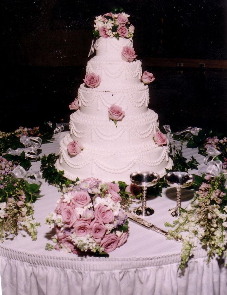 a white wedding cake with pink flowers and greenery on the table at a reception