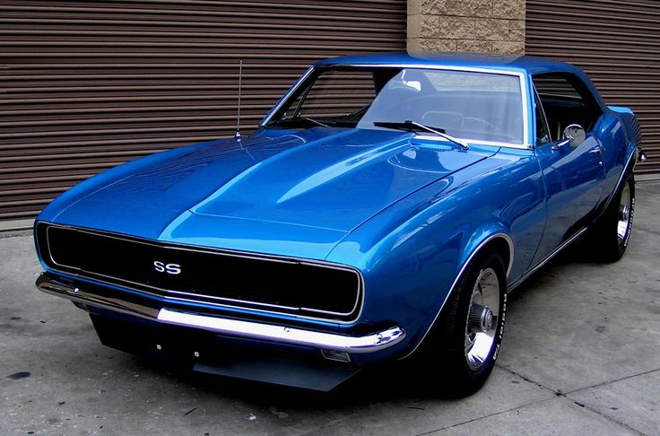 a blue muscle car parked in front of a garage door