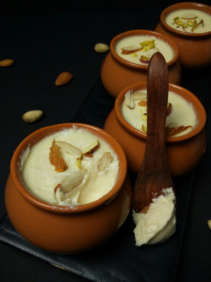 four small bowls filled with food on top of a black table next to a wooden spoon