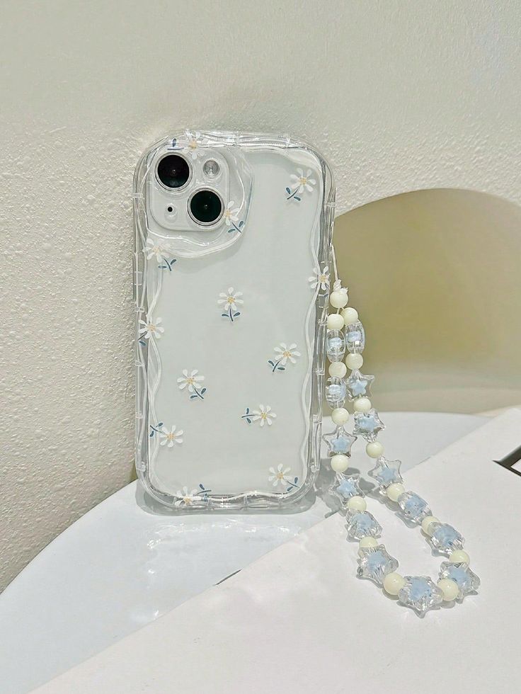 an iphone case with flowers and pearls attached to it sitting on a table next to a beaded necklace