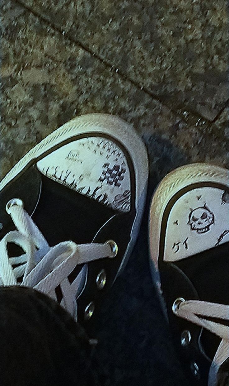 two black and white shoes are sitting on the ground with their laces undone to them