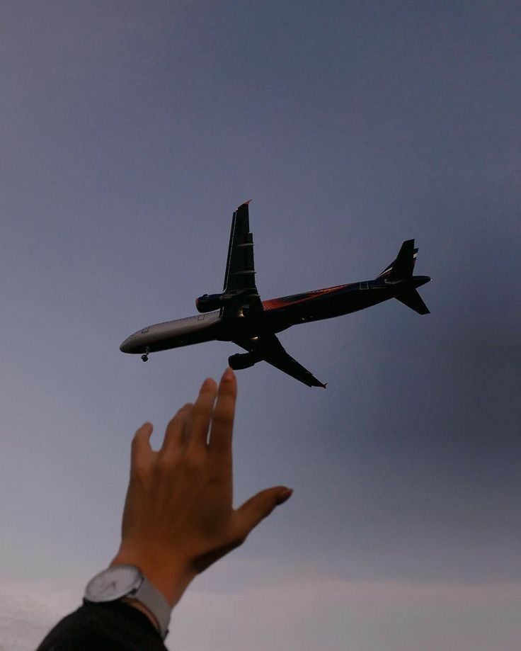 a person's hand reaching up to an airplane in the sky