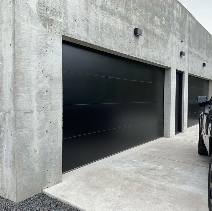 a black car is parked in front of a building with two garage doors on it