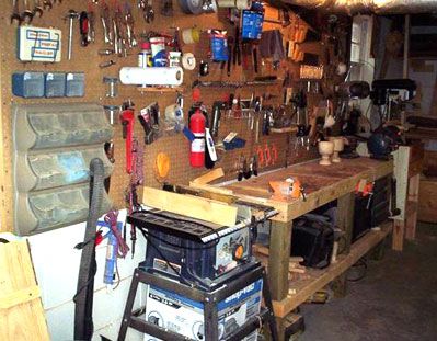 a workbench with many tools hanging on the wall and various other items in it