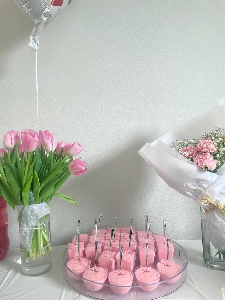 pink cupcakes are arranged on a table with flowers and balloons in the background