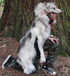 a person with a wolf mask sitting in front of a tree and wearing camouflage pants