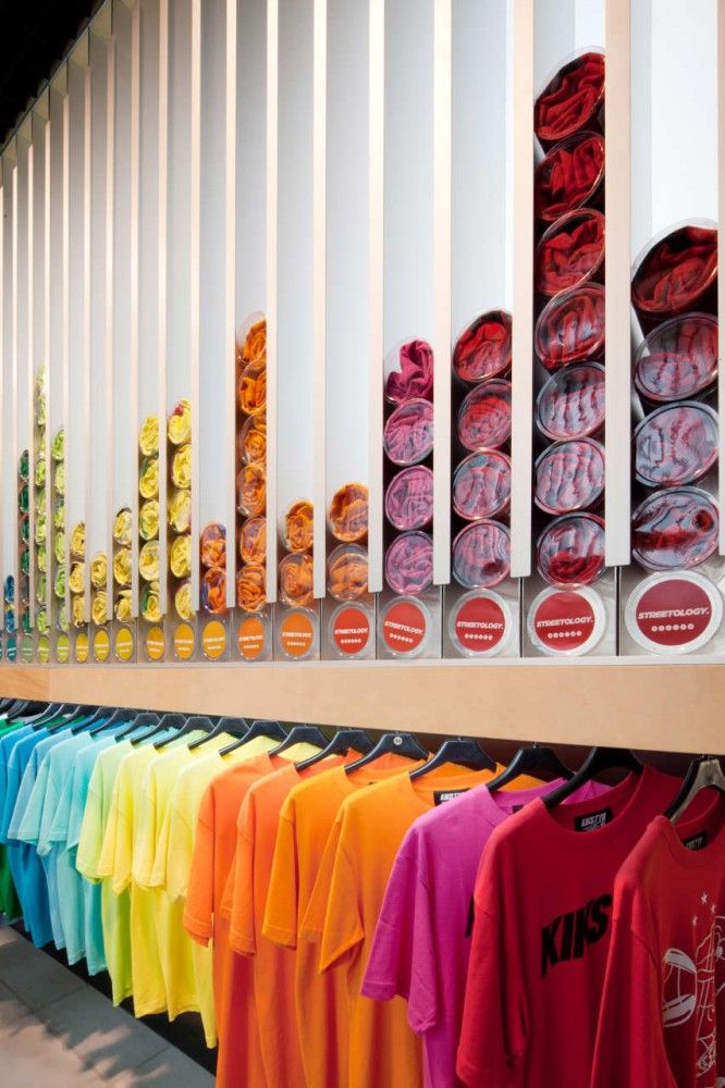 colorful shirts and t - shirts are on display in a store with white vertical blinds