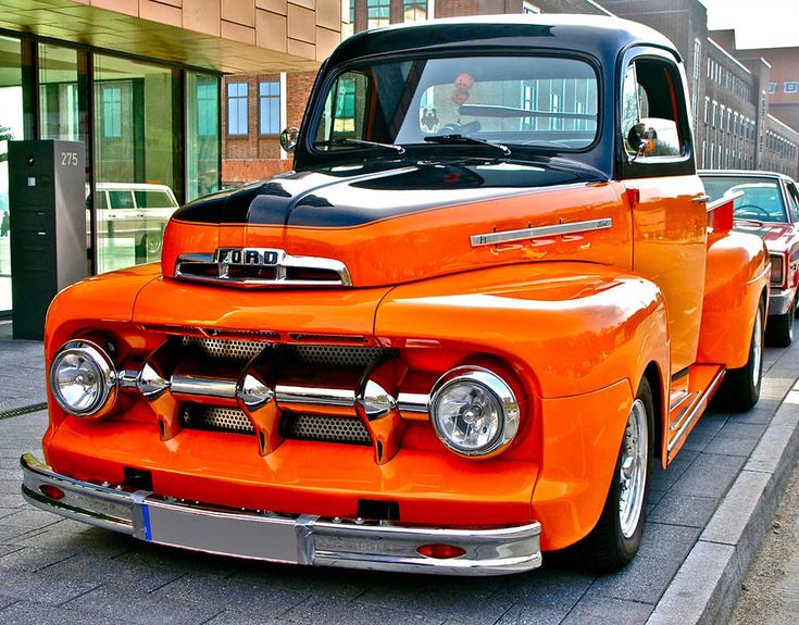 an orange and black truck parked on the side of a road next to another car