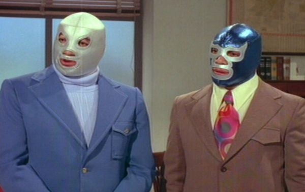 two men in suits and masks stand next to each other, one wearing a blue suit