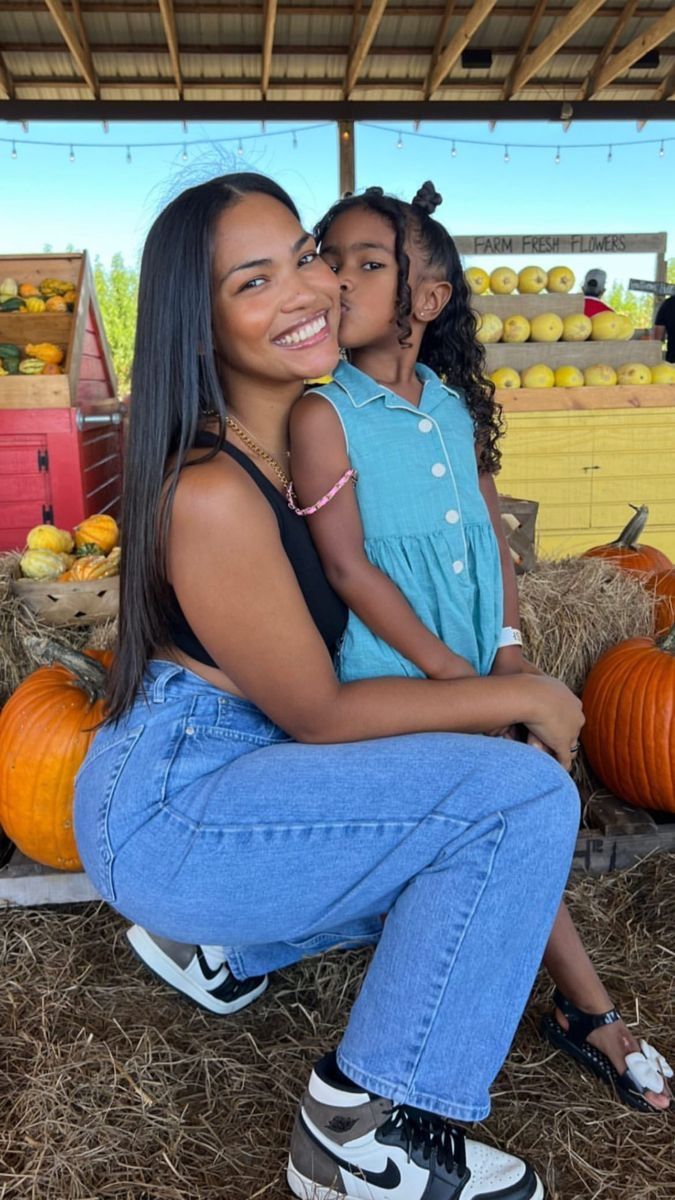 a mother and daughter sitting on hay with pumpkins in the background