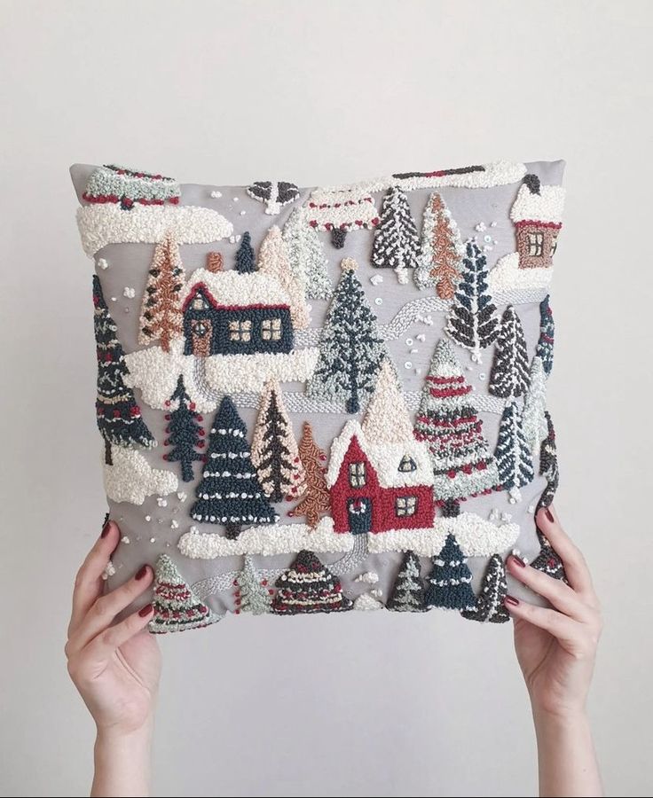 someone is holding up a pillow with christmas trees and houses on it in front of a white wall