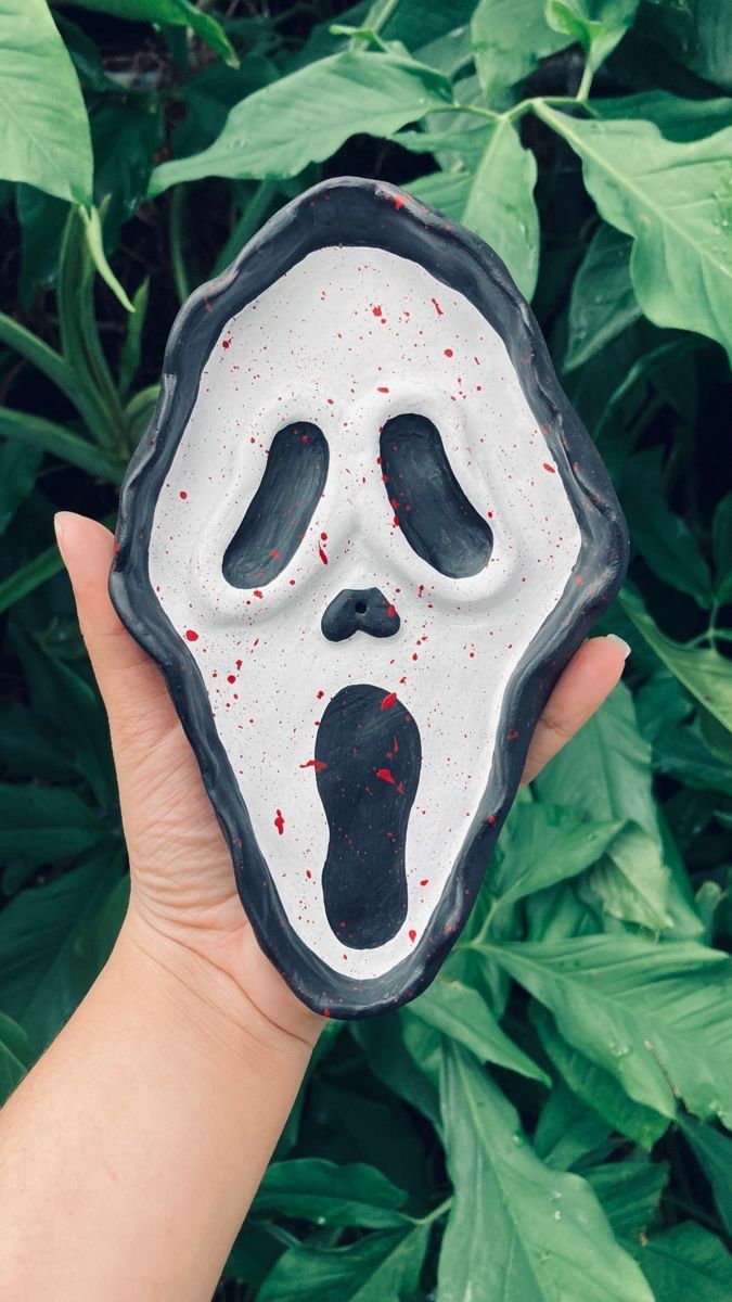 someone holding up a fake mask with red paint on it in front of green leaves