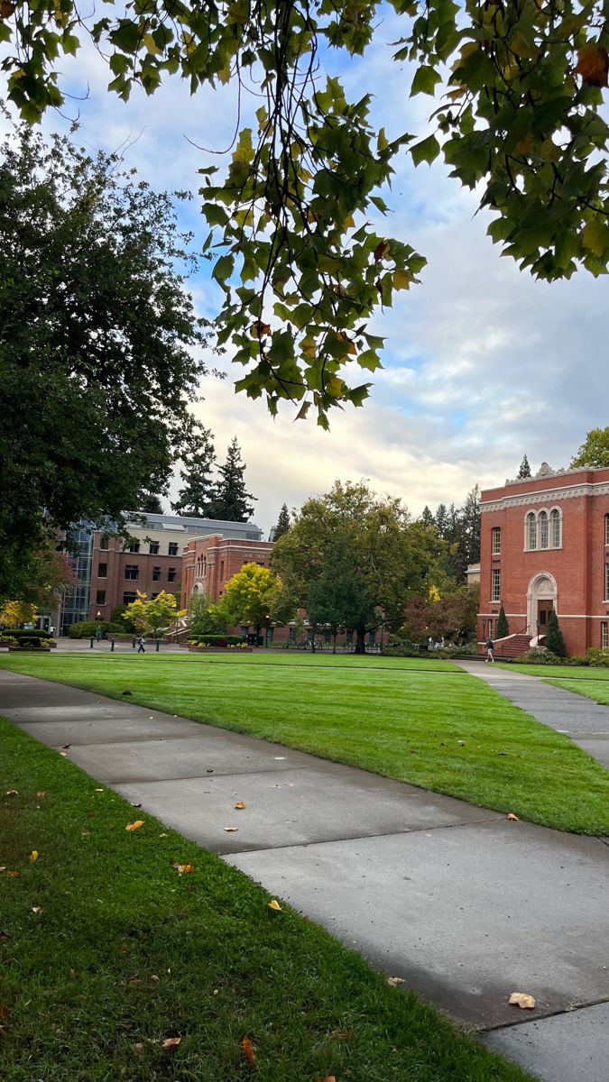 the grass is green in front of an old red brick building with trees on both sides