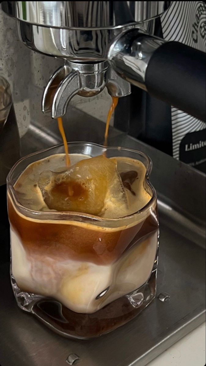 an espresso being poured into a glass cup with ice and coffee in it