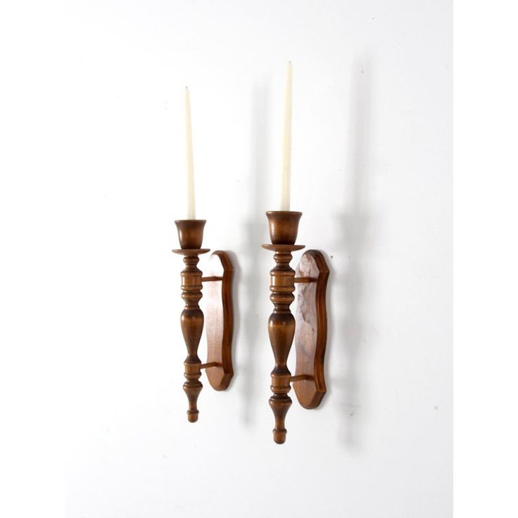 two wooden candlesticks on a white wall with one candle in between them and the other