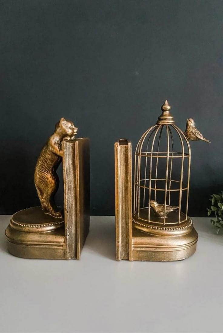 two golden figurines are next to a birdcage with a squirrel on it