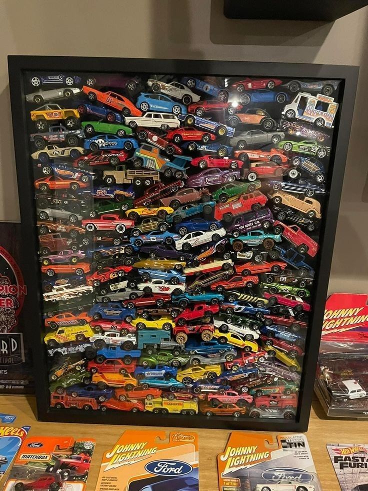 a collection of hot wheels cars on display in a black shadow box with wooden flooring