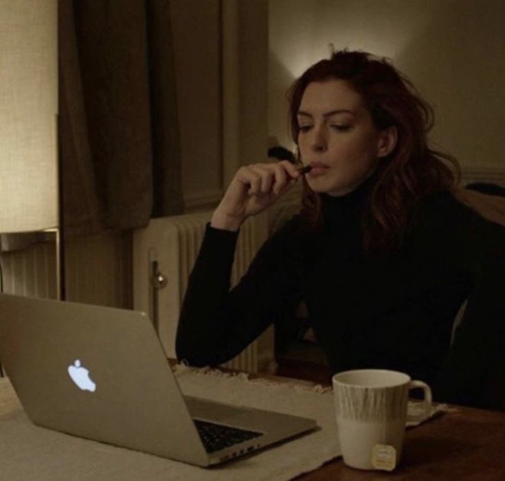 a woman sitting at a table with an apple laptop in front of her, while looking at the screen