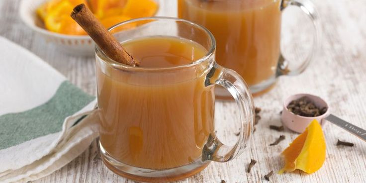 two mugs filled with cinnamon sitting on top of a table next to orange slices