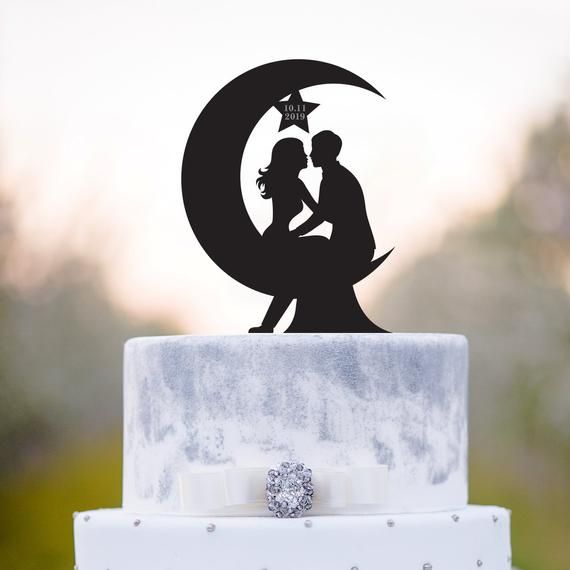 a wedding cake topper with the silhouette of a bride and groom kissing in front of a full moon