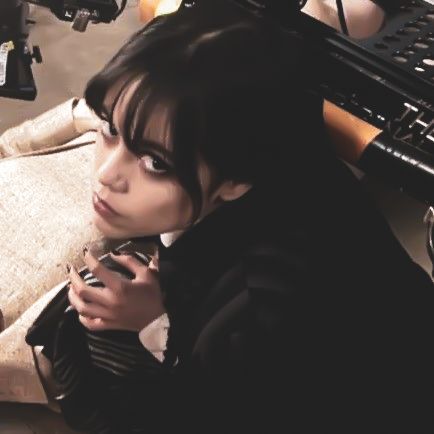 a woman holding a cell phone while sitting next to a keyboard and computer monitor on top of a desk