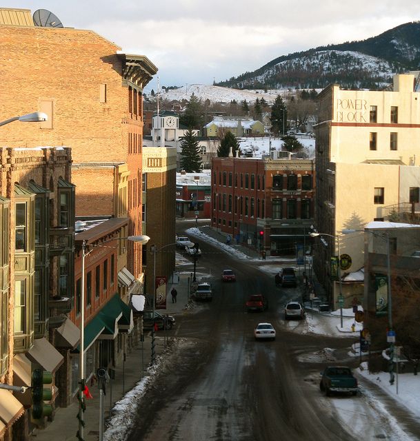 a city street filled with lots of traffic next to tall brick buildings and snow covered mountains