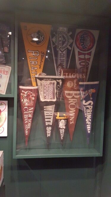 an assortment of pennants are on display in a glass case with green walls behind them