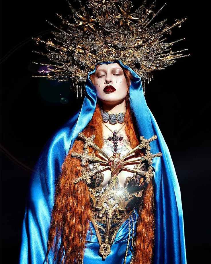 a woman with long red hair wearing a blue dress and headdress is standing in front of a black background