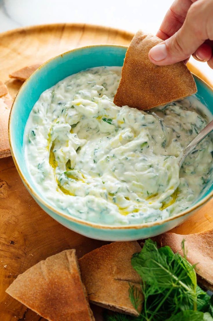 a person dipping something into a bowl of dip with tortilla chips on the side