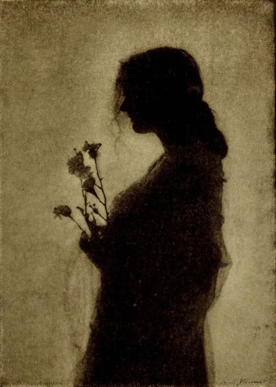 the silhouette of a woman holding flowers in her hand