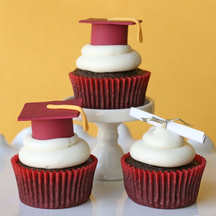 three cupcakes with white frosting and graduation caps on top, sitting on a cake stand