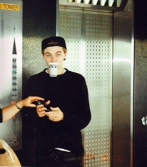 a man standing in front of an elevator holding something to his mouth and looking at the camera