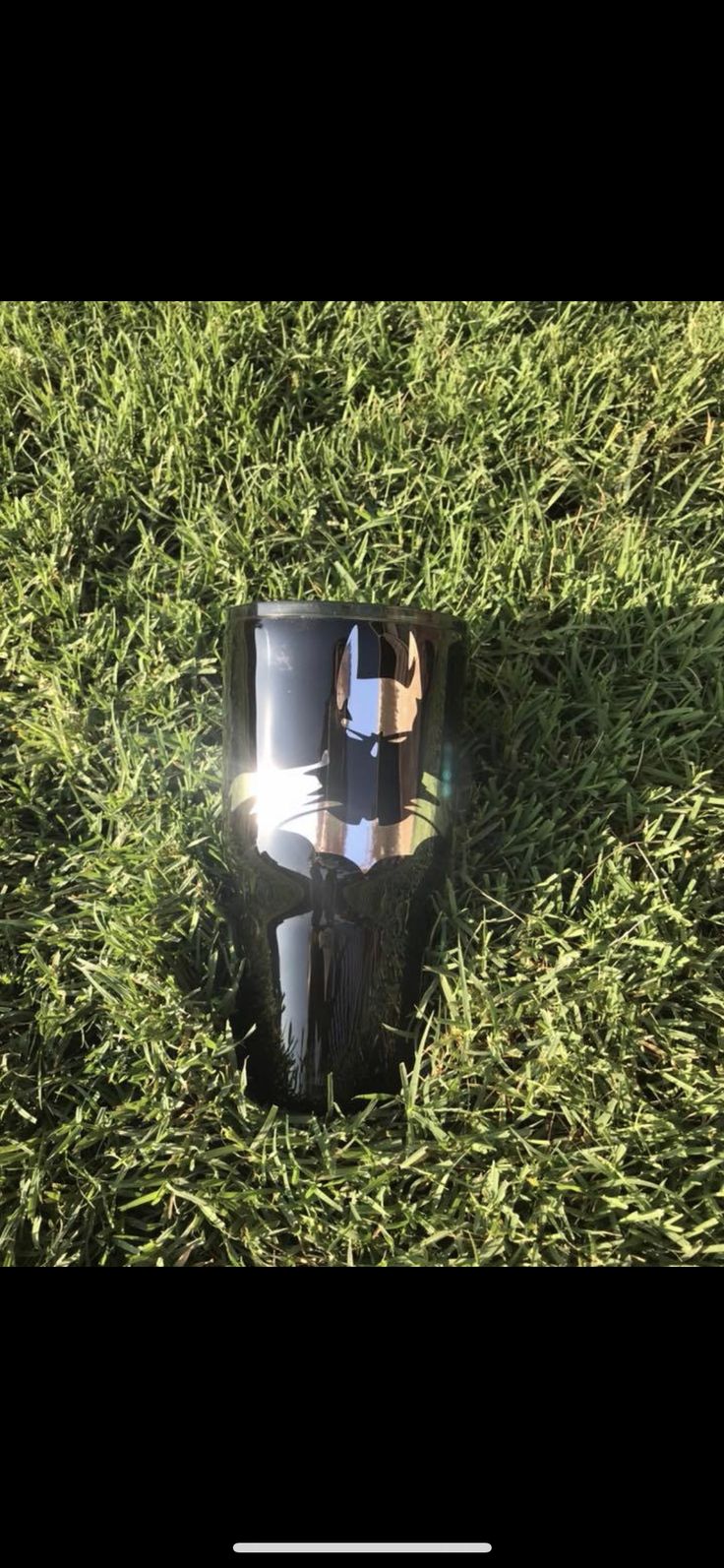 a black object laying in the grass with its reflection on it's side,