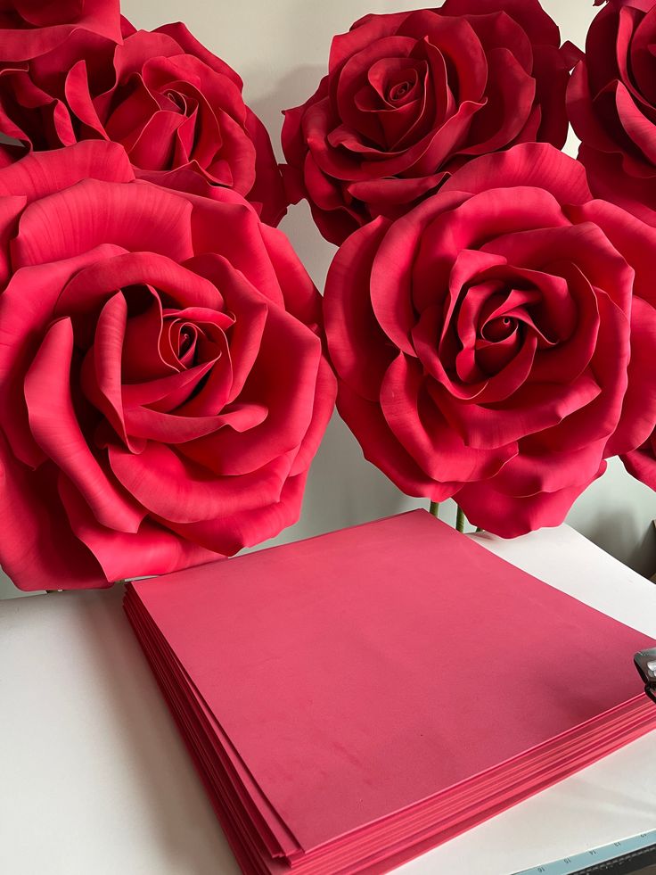 several red roses sitting on top of a table next to a pink notebook and pen