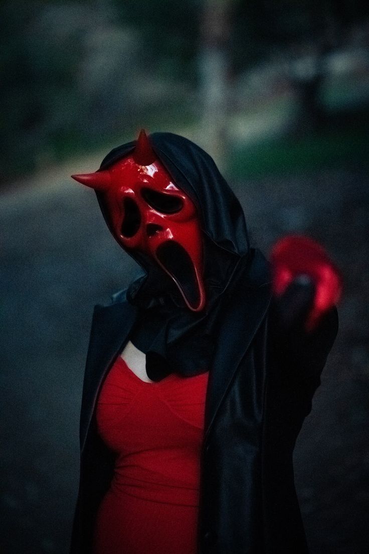 a woman wearing a devil mask and holding a red object in her hand with the mouth open