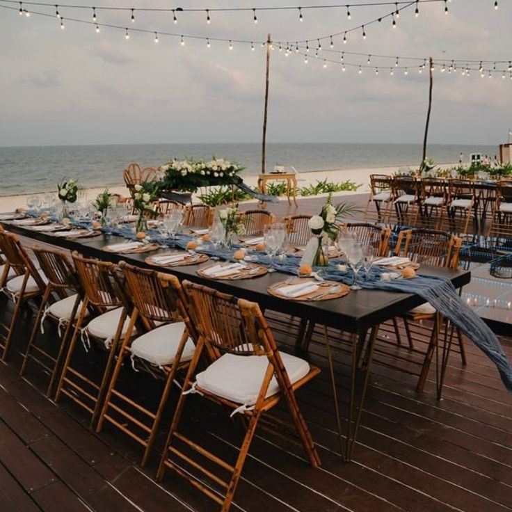 a long table set up on the beach for an outdoor wedding reception with string lights strung over it