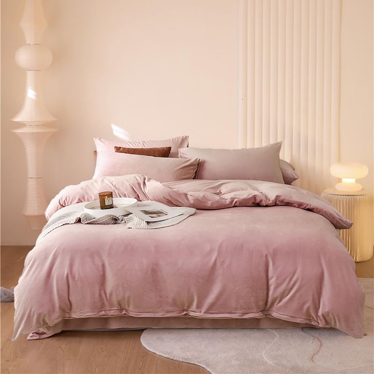 a bed with pink sheets and pillows on top of it next to a white lamp